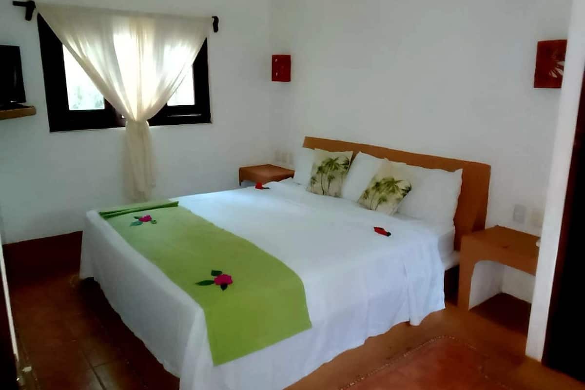 Un dormitorio con cama, mesita de noche, ventana con cortinas e interruptor de luz en la pared.