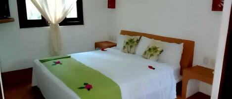 A bedroom with a bed, a nightstand, a window with curtains, and a wall-mounted light switch.