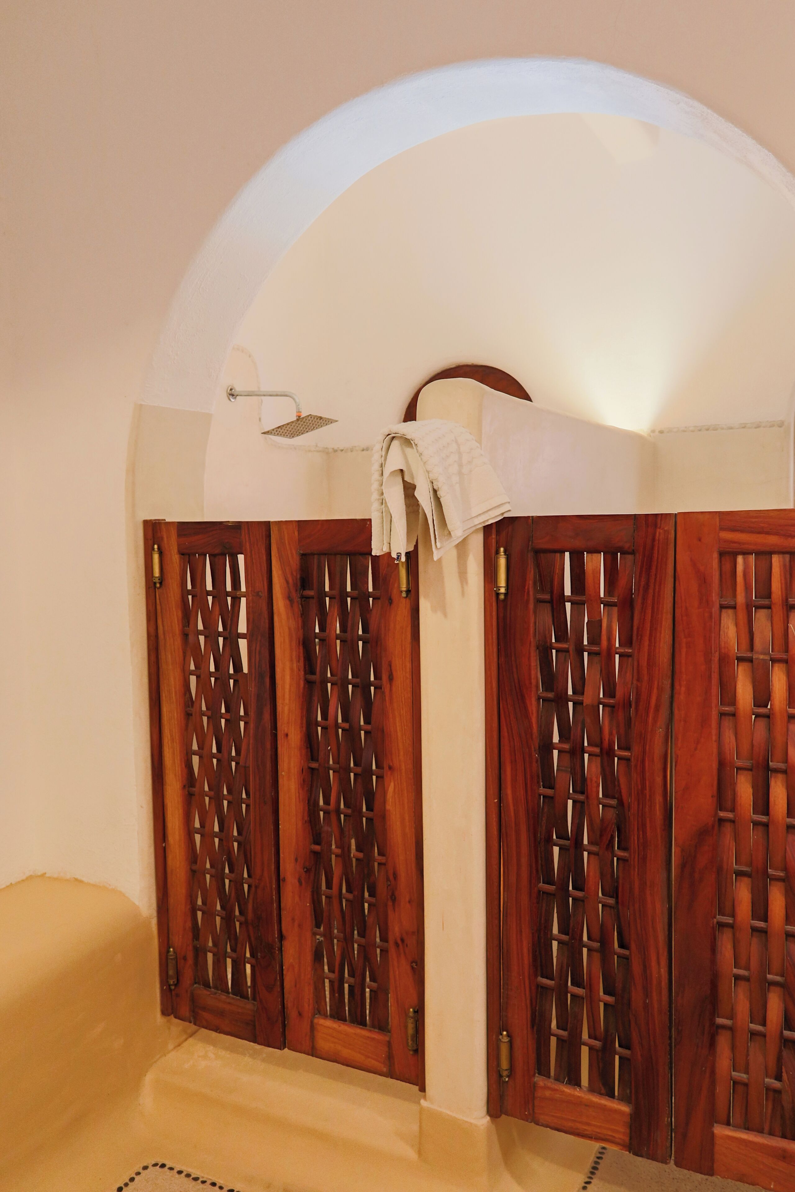 A bathroom with wooden lattice doors, a towel hanging on a hook, and a showerhead.