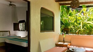 A room with two beds, a small table, and a window overlooking greenery.