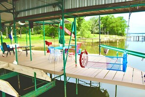 Een overdekt buitengebied met een houten terras, stoelen en een tafel.