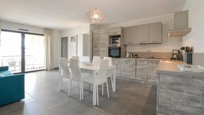 A modern kitchen with white cabinets, a built-in oven, and a dining area with white chairs. - 2 bedroom nice apartment in Algajola (Algajola)