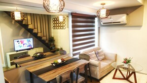 A modern living room with a dining area, a sofa, a glass coffee table, and a TV on a cabinet. - Fort Victoria BGC Netflix 25M WiFi (Taguig)