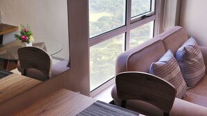 A modern room with a sofa, a dining table, and a view of a green landscape through large windows. - Fort Victoria BGC Netflix 25M WiFi (Taguig)