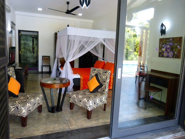 A room with a bed, a sitting area with patterned chairs, a small table, and a glass partition. - Luxurious villa 3 kms from beautiful beaches and restaurants and Galle fort (Akmeemana)