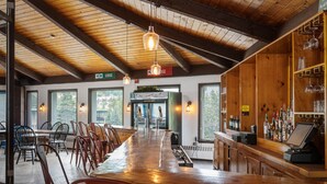 A bar area with wooden ceiling beams, a long counter, and multiple chairs. - The Lodge at Mount Snow (West Dover)
