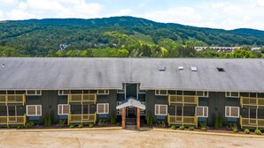 A motel with a central entrance, multiple balconies, and a view of a forested hill in the background. - The Lodge at Mount Snow (West Dover)