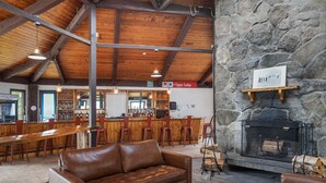 A rustic interior with a stone fireplace, wooden ceiling beams, a bar area, and leather seating. - The Lodge at Mount Snow (West Dover)