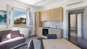 Een moderne keuken met houten kastjes, een betegelde spatwand en een inbouwoven. Er is een zithoek met een tafel en stoelen, en een bank met uitzicht op de omgeving.