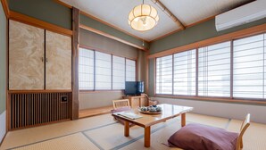 Una habitación japonesa tradicional con suelo de tatami, una mesa baja, un banco acolchado y puertas correderas.