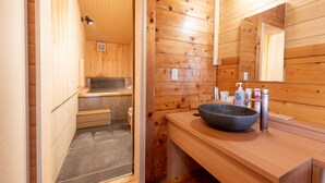 Un interior de madera con suelo de baldosas de piedra, un lavabo grande con lavamanos y un espejo encima.