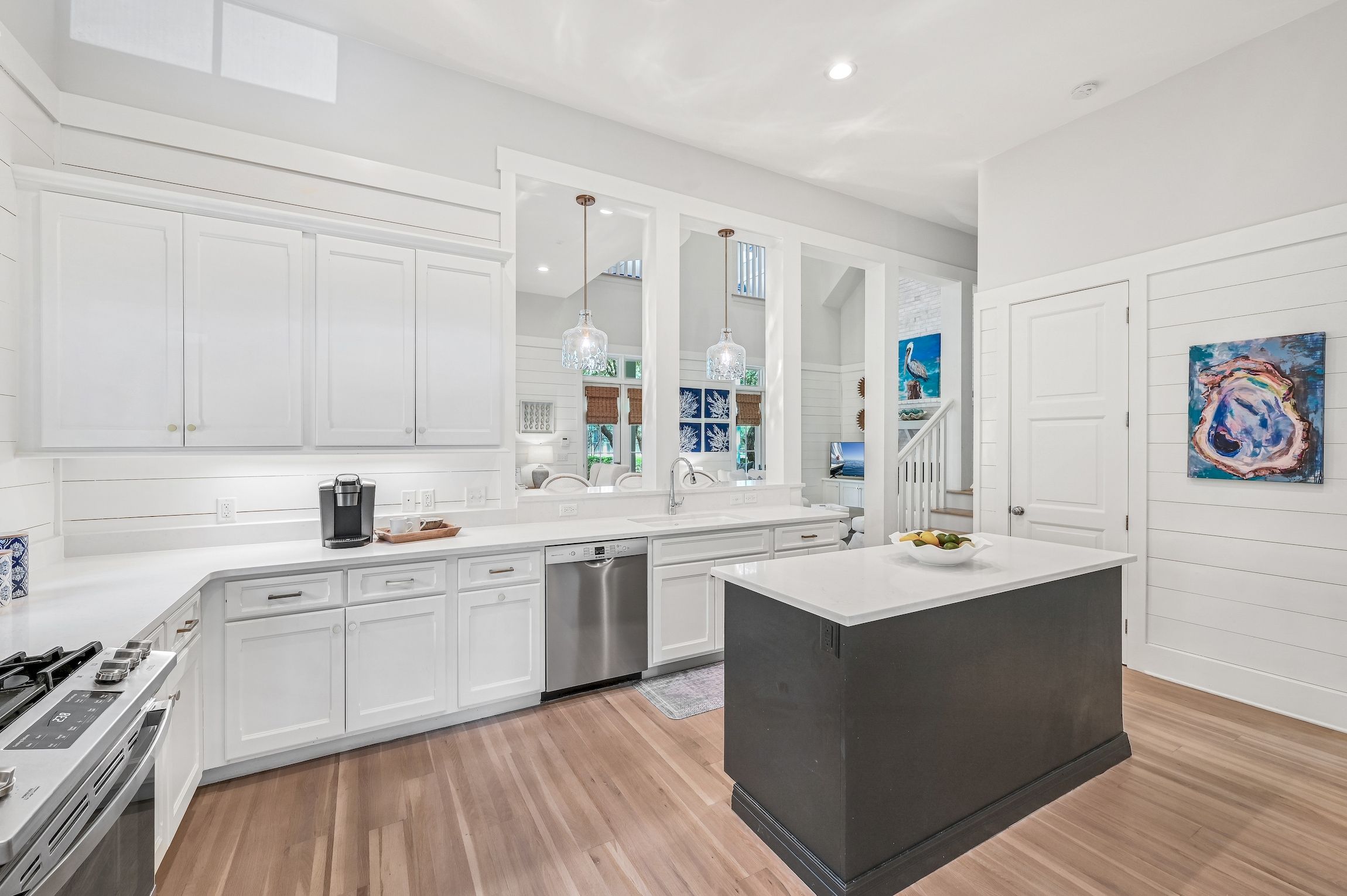 A modern kitchen with white cabinetry, a central island, stainless steel appliances, and decorative elements like artwork and pendant lights.