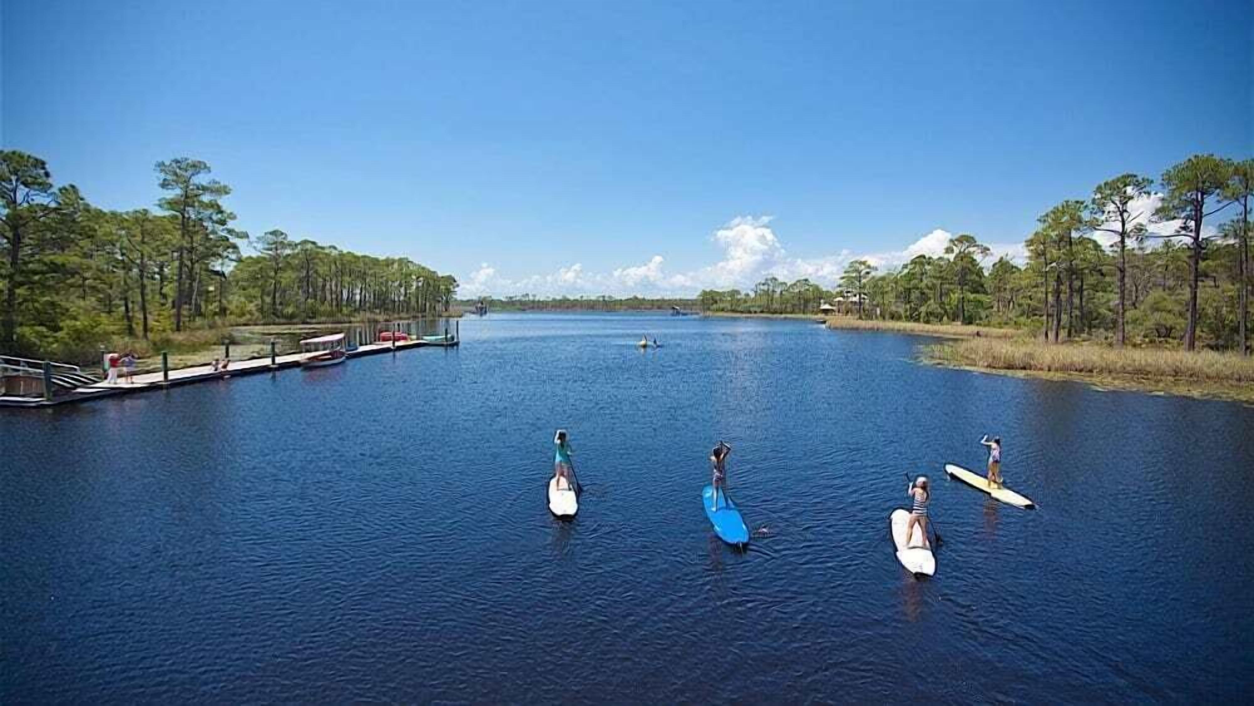 A calm river with paddleboards, a dock, and a forested shoreline.