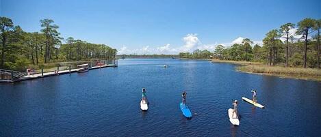 A calm river with paddleboards, a dock, and a forested shoreline.