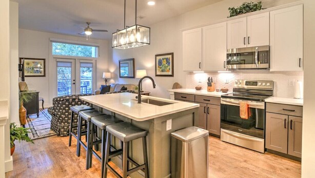 A modern kitchen with a central island, stainless steel appliances, and a seating area with a sofa and chairs.