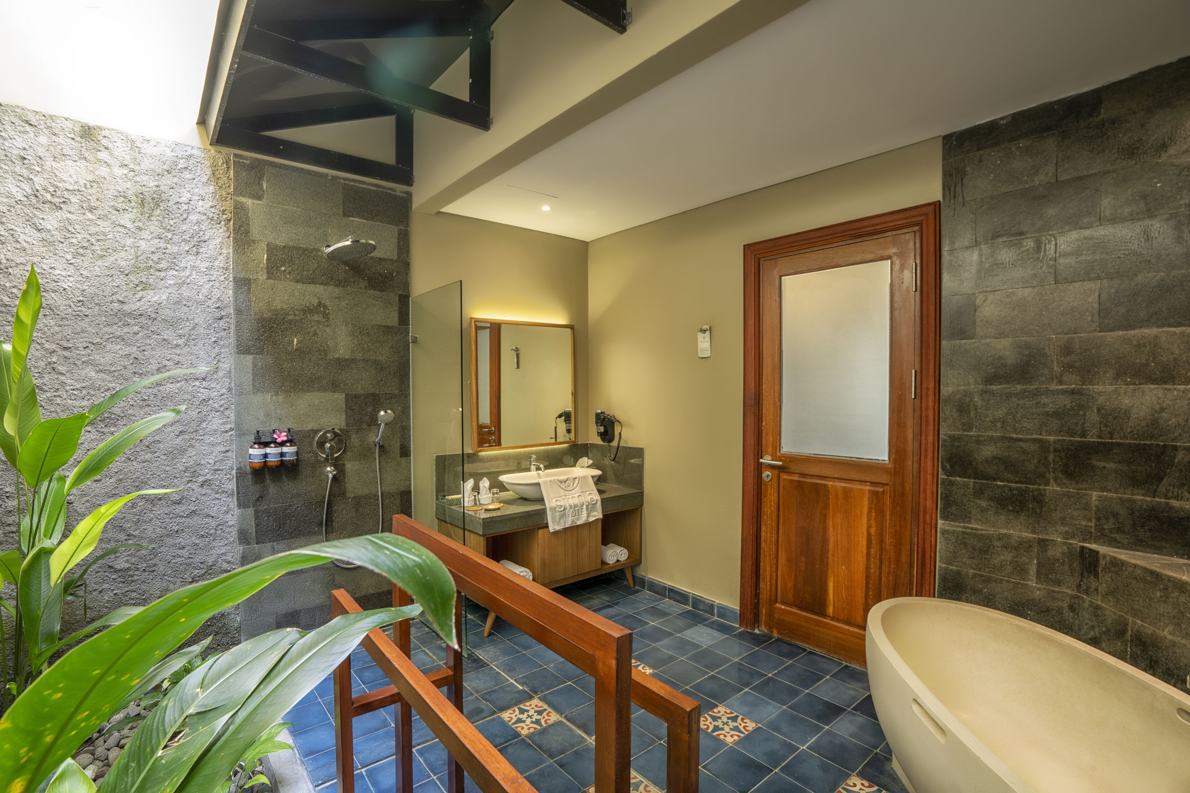 Un baño con bañera, un banco de madera, un lavamanos y un espejo.