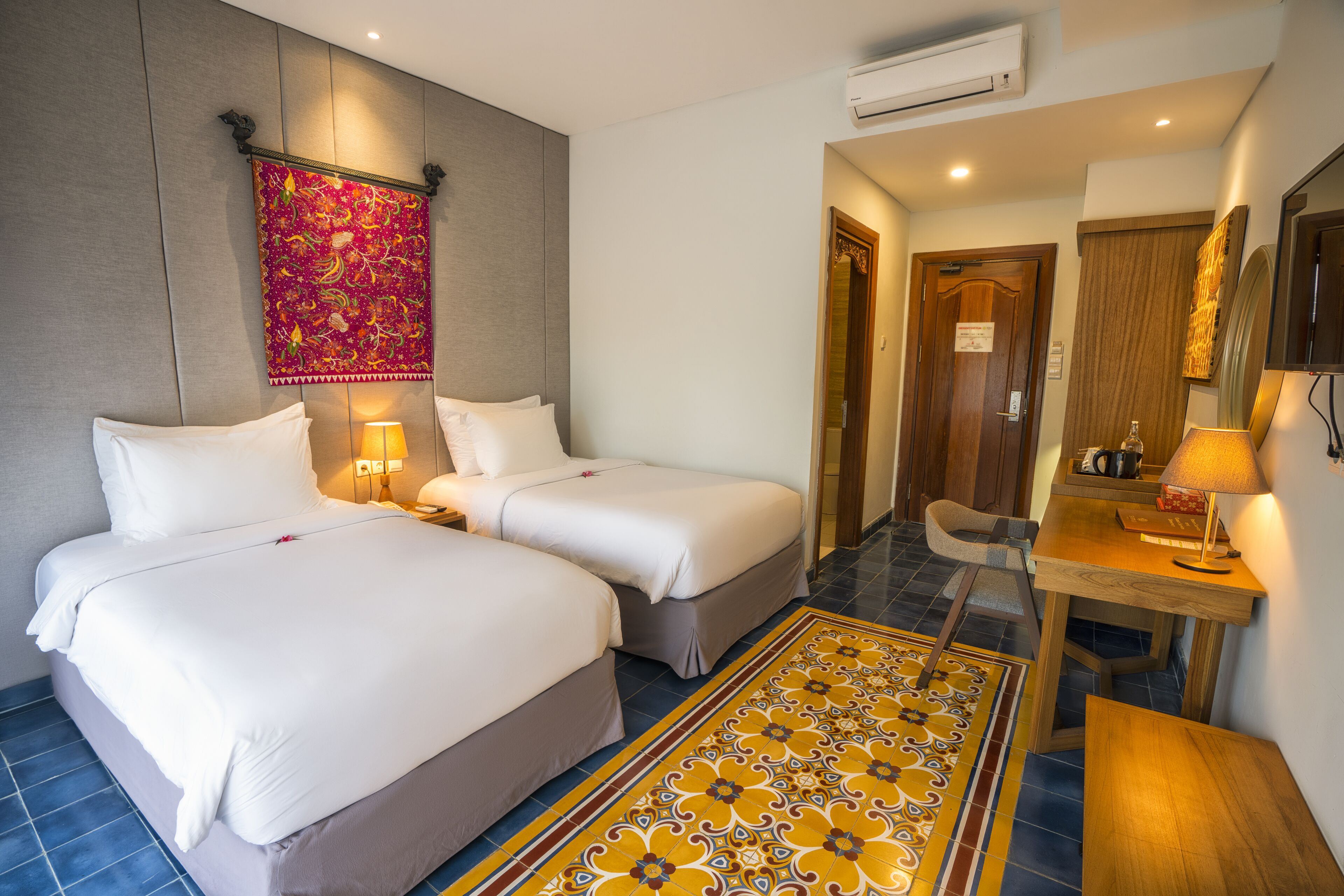 A hotel room with two beds, a desk, a chair, and a patterned rug.