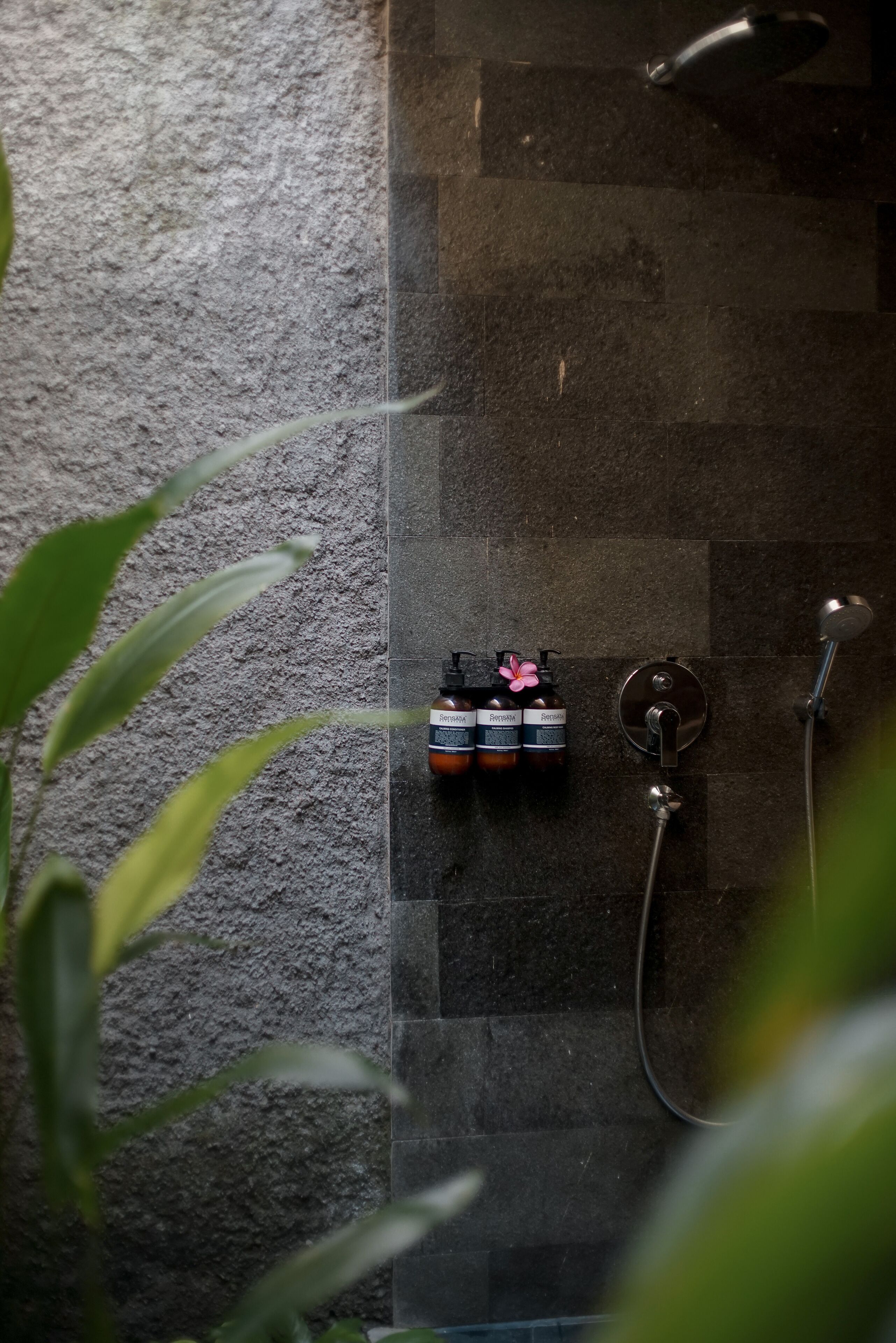 Baño con pared de piedra, ducha y tres botellas de champú.