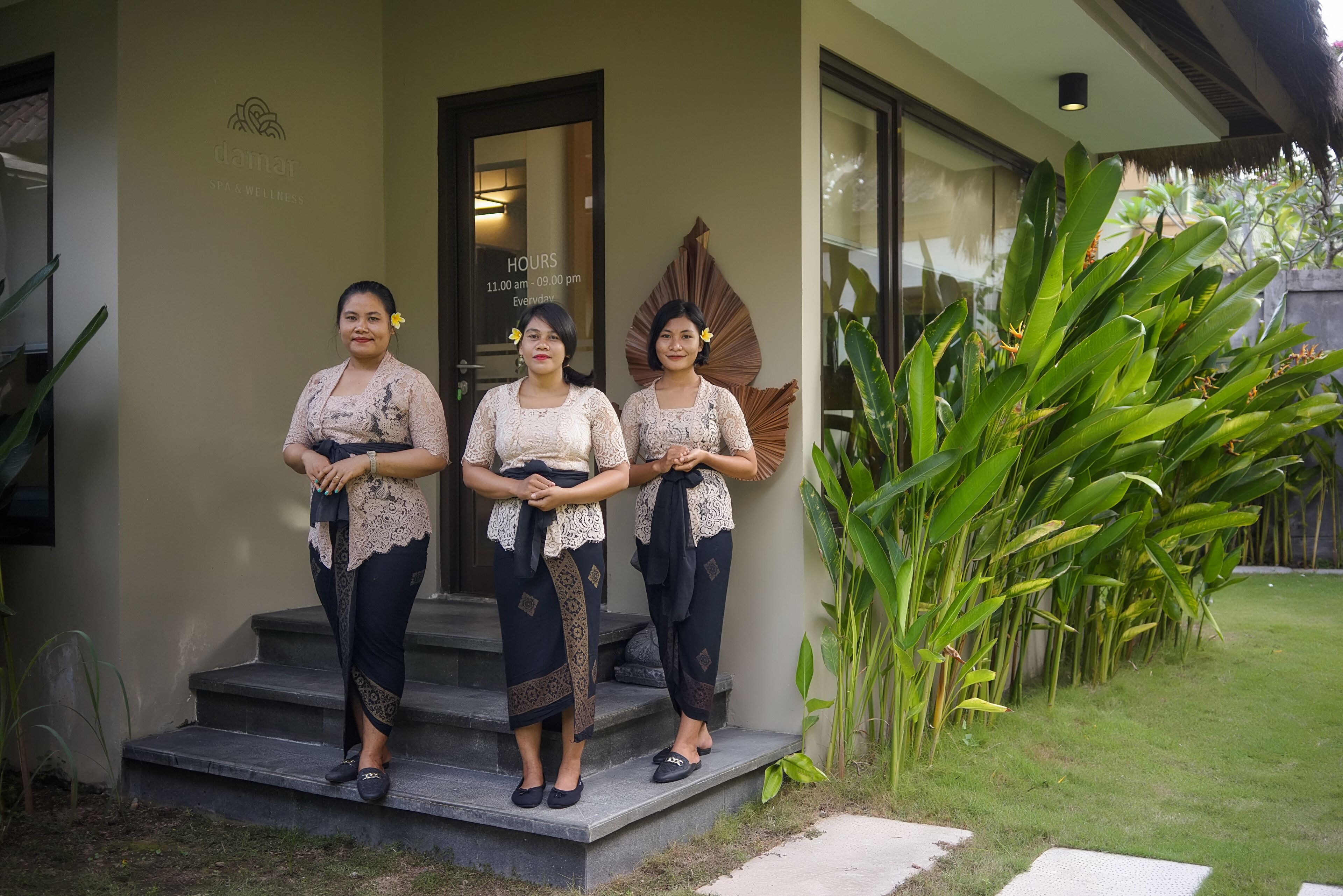 Three women standing on a staircase outside a building with a sign indicating 'Hours 11:00 am - 09:00 pm Every day'.