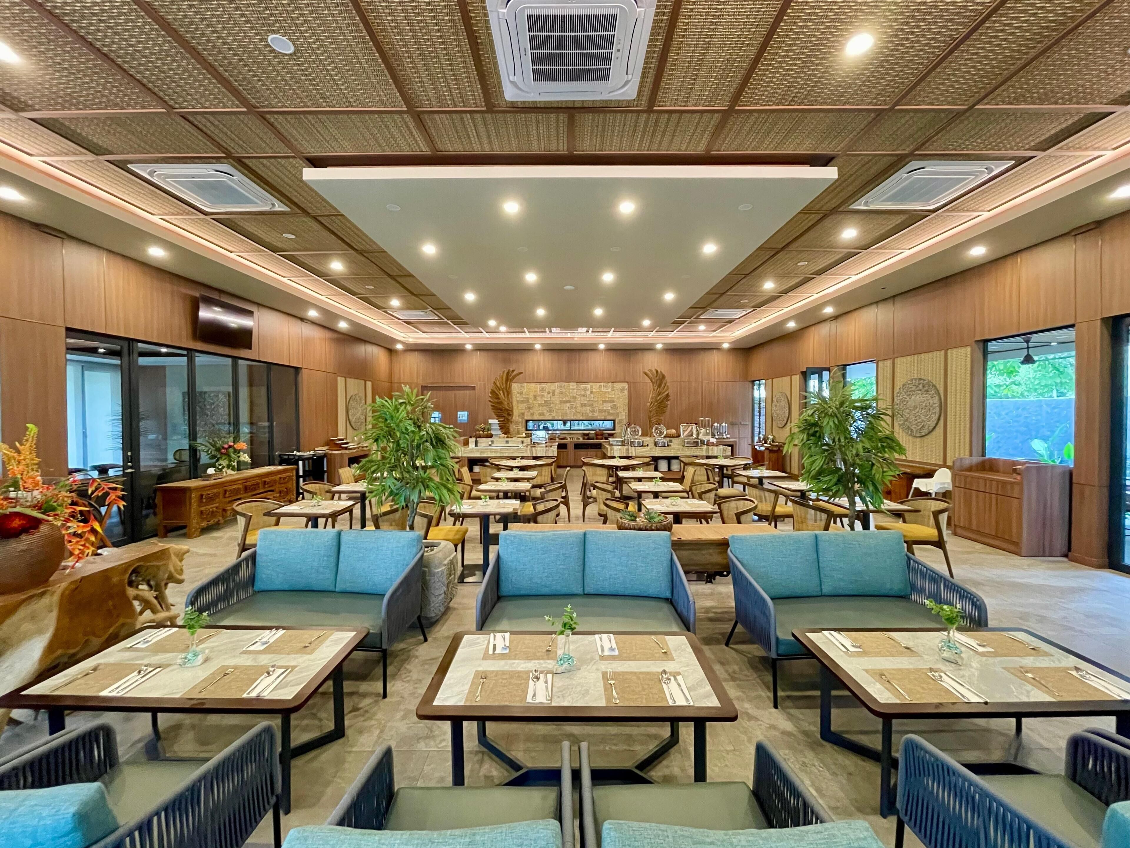 A spacious restaurant with multiple dining tables, blue cushioned seating, and a modern ceiling design.