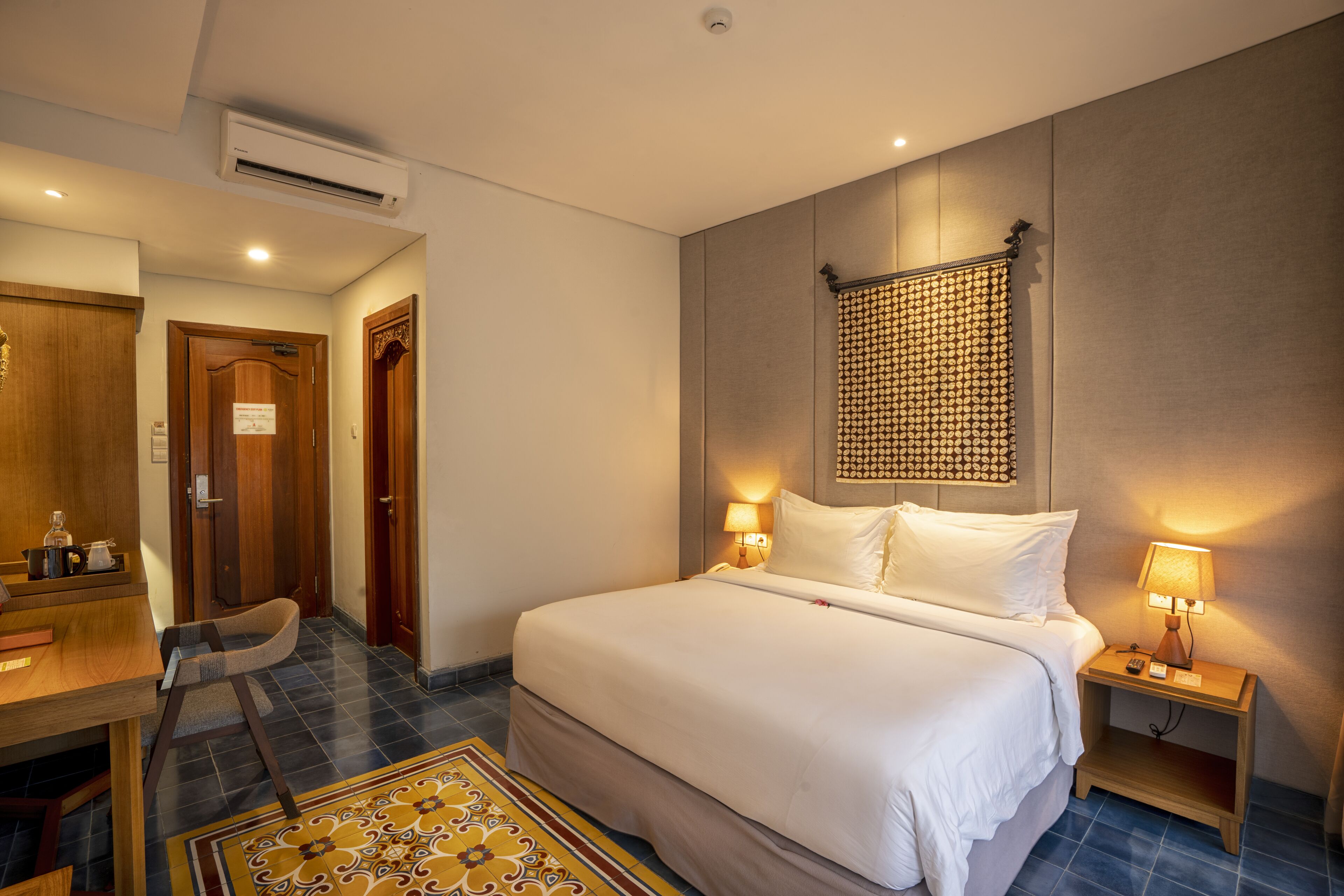 A hotel room with a large bed, bedside tables with lamps, a desk with a chair, and a patterned rug.