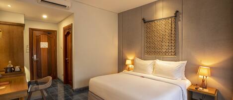 A hotel room with a large bed, bedside tables with lamps, a desk with a chair, and a patterned rug.