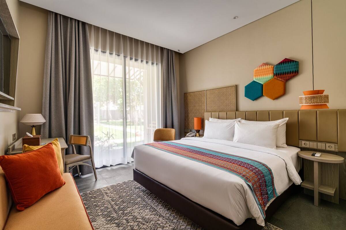 Ein Hotelzimmer mit einem großen Bett, einer Couch, einem Schreibtisch und Blick ins Freie.