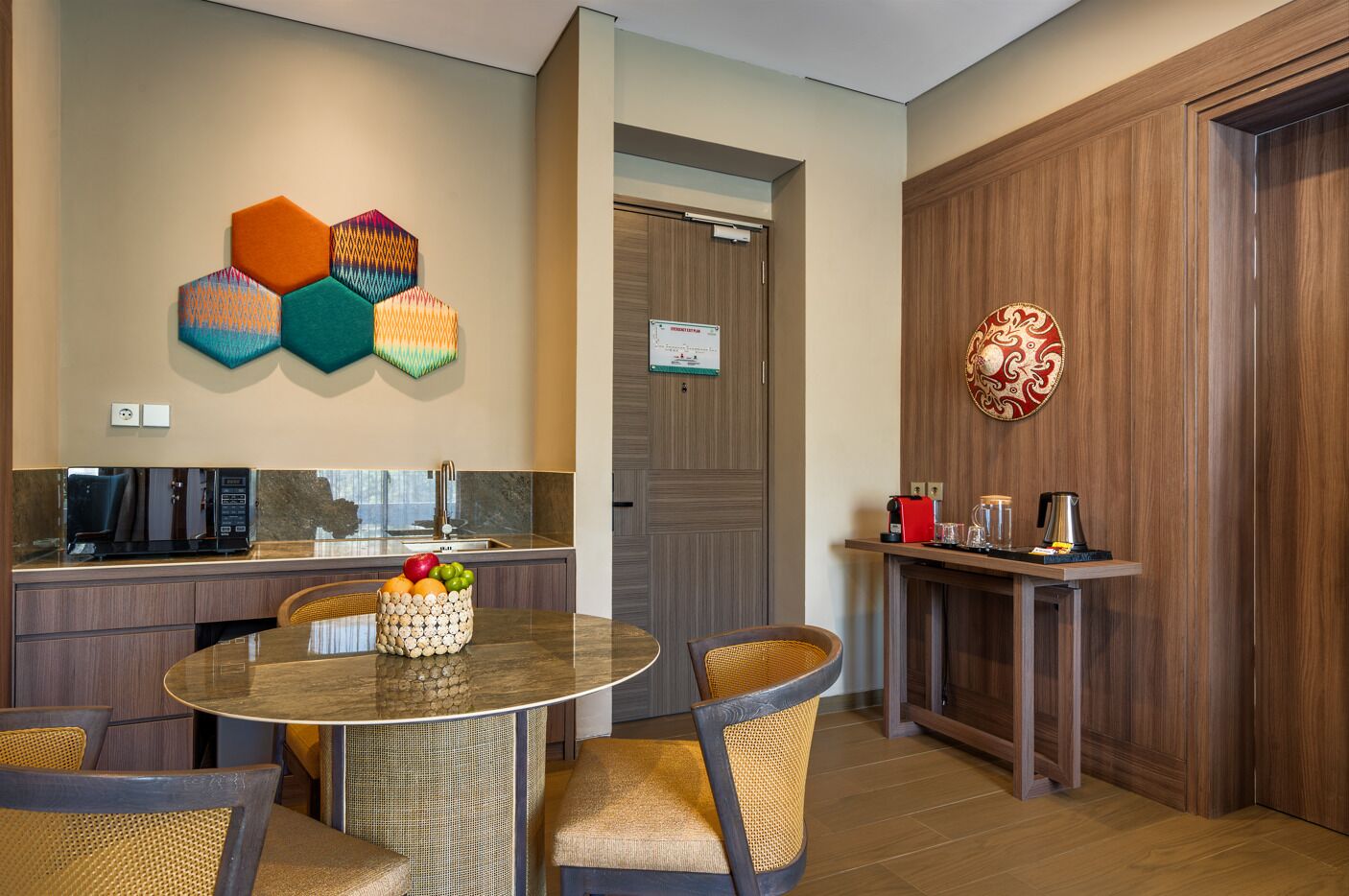 A modern kitchen with a round dining table, wicker chairs, and a fruit basket.