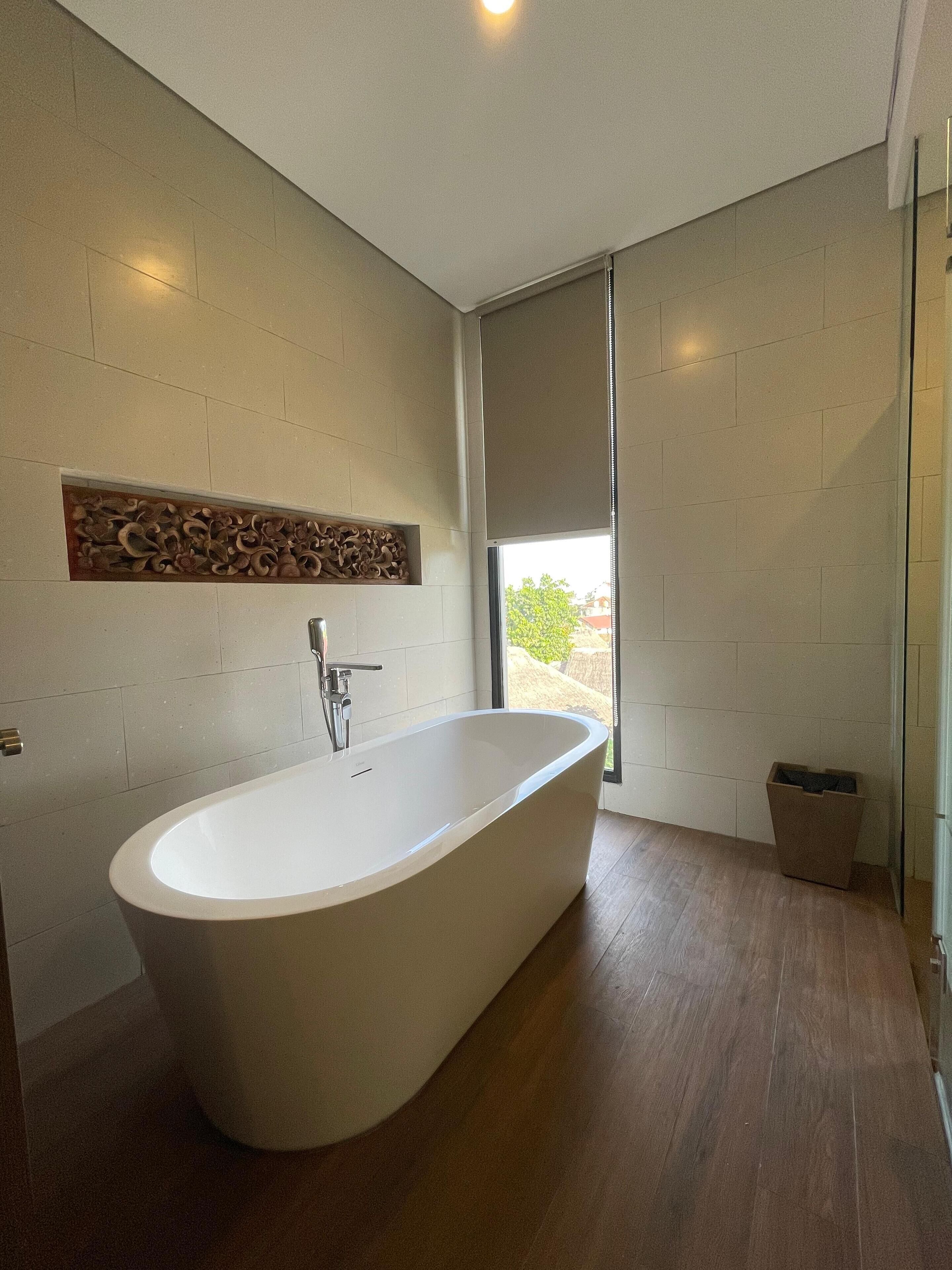 A modern bathroom with a freestanding bathtub, a wooden wall decor, and a view through a large window.