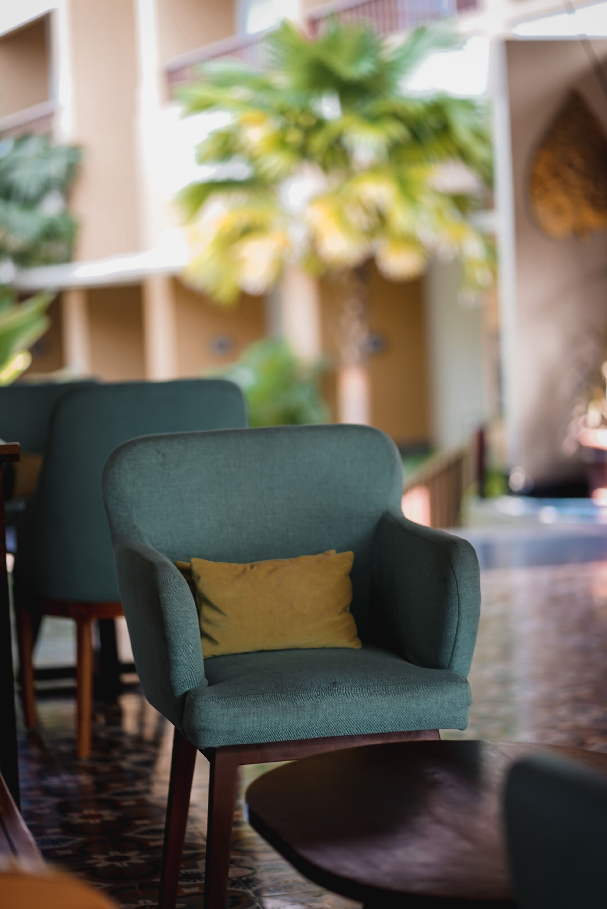 A green armchair with a yellow pillow in a hotel lobby.