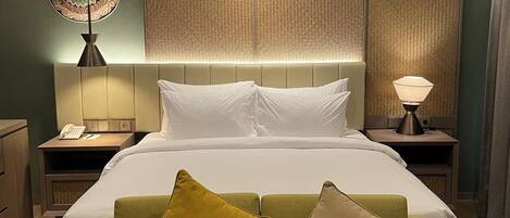 A hotel room with a bed, a green sofa, a bedside table with a lamp, and a decorative wall panel.