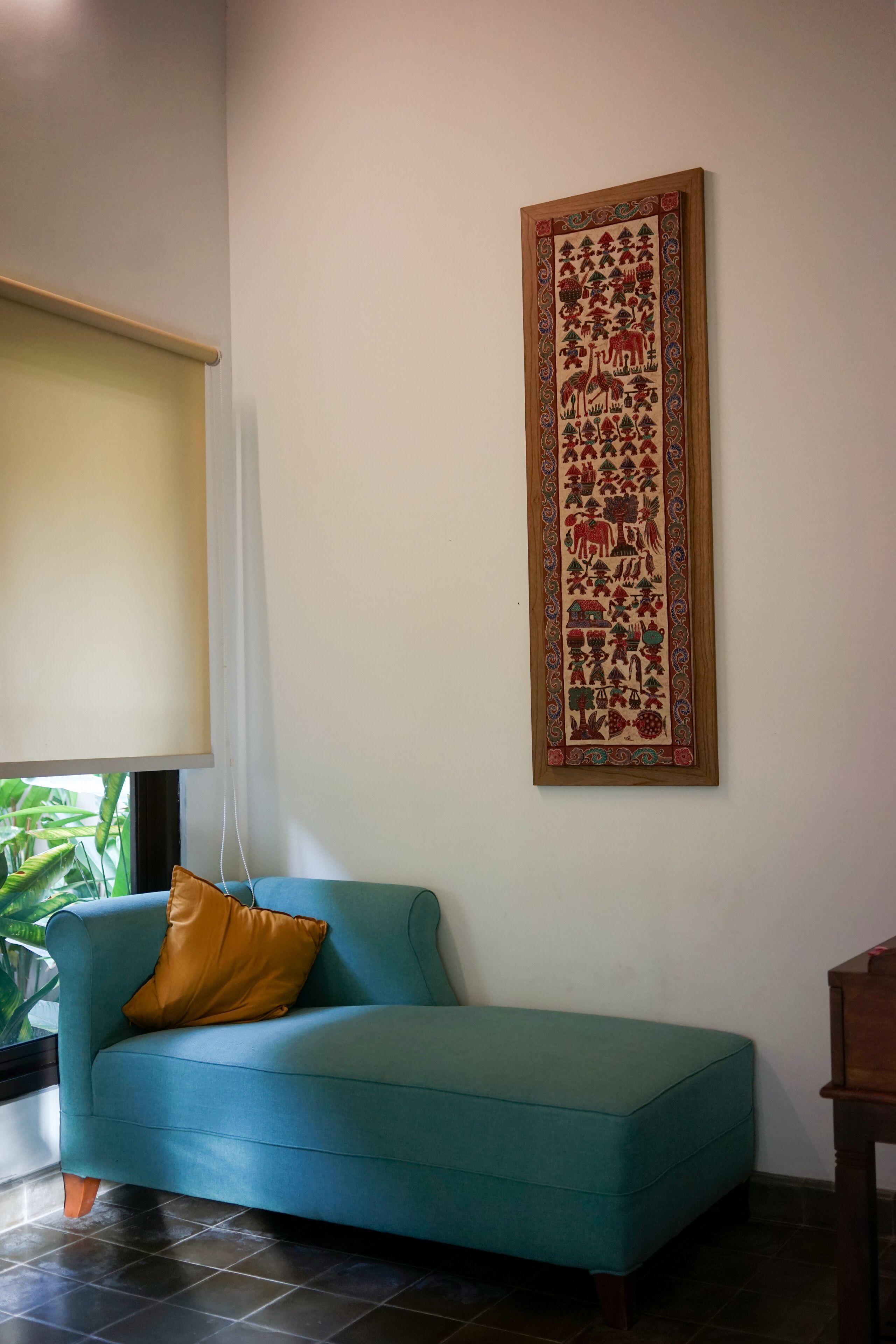 Un canapé de couleur bleu-vert avec un coussin marron, une table en bois et une tapisserie encadrée accrochée au mur.
