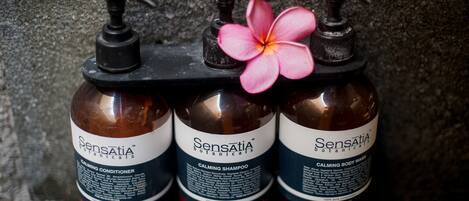 Three bottles of Sensatia Botanicals calming products on a black pump dispenser against a textured wall.