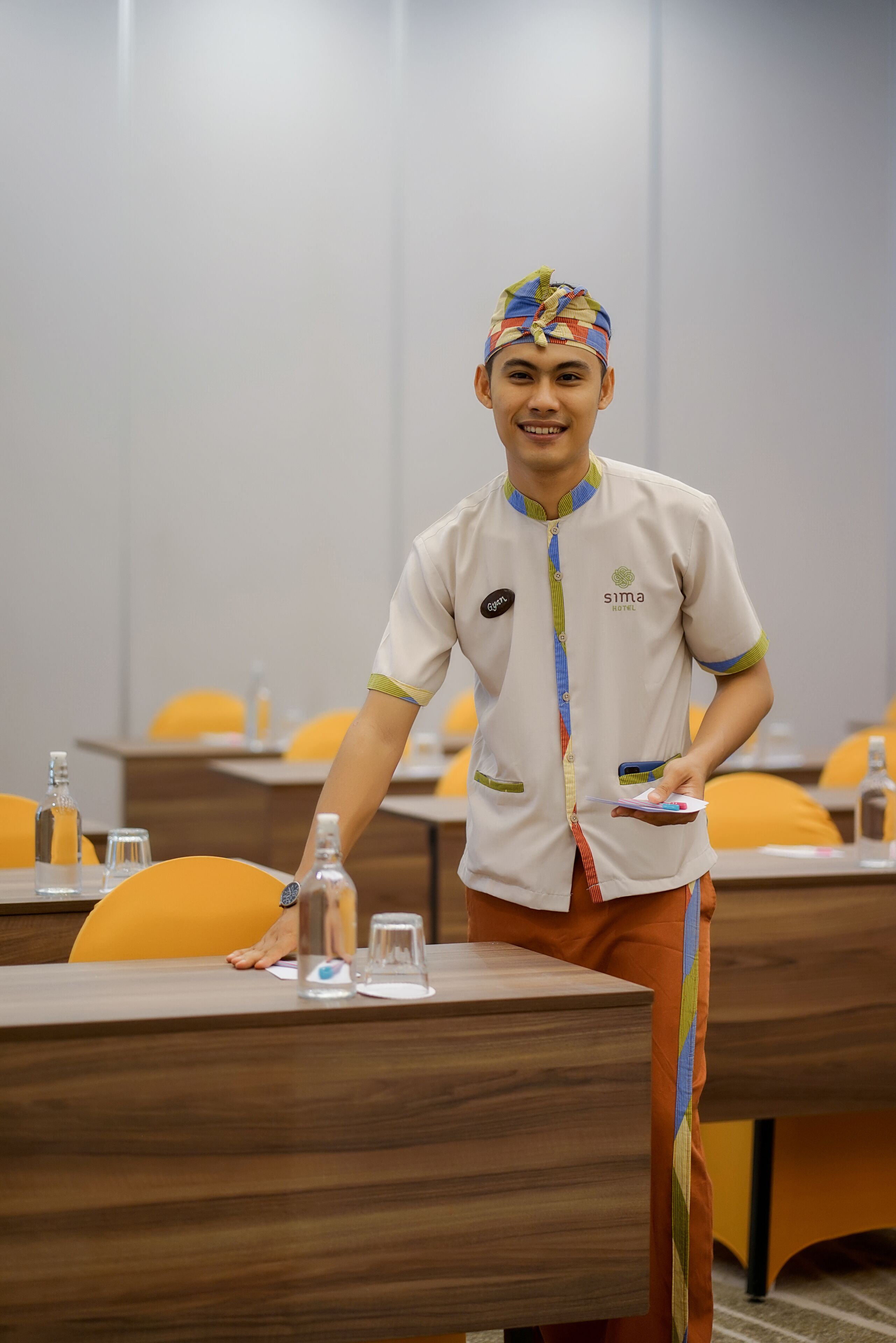 A hotel staff member in uniform standing by a table with a glass of water and a bottle.
