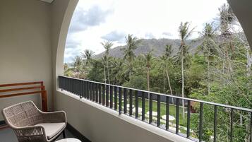 Un balcón con mobiliario de mimbre y vistas a un paisaje exuberante con palmeras y montañas.