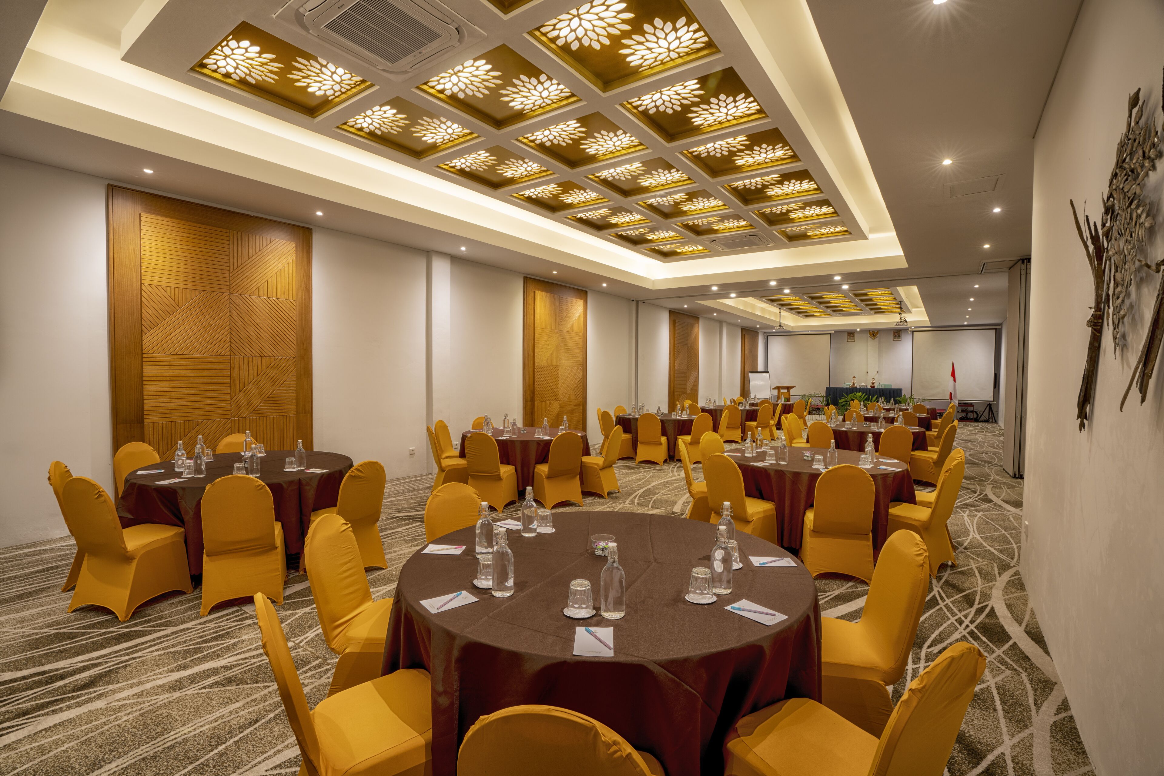 A conference room with multiple tables, yellow chairs, and a patterned ceiling.