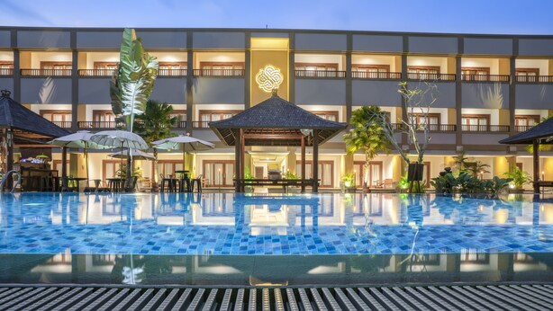 Un hotel con una piscina grande, mobiliario exterior y una fachada bien iluminada.