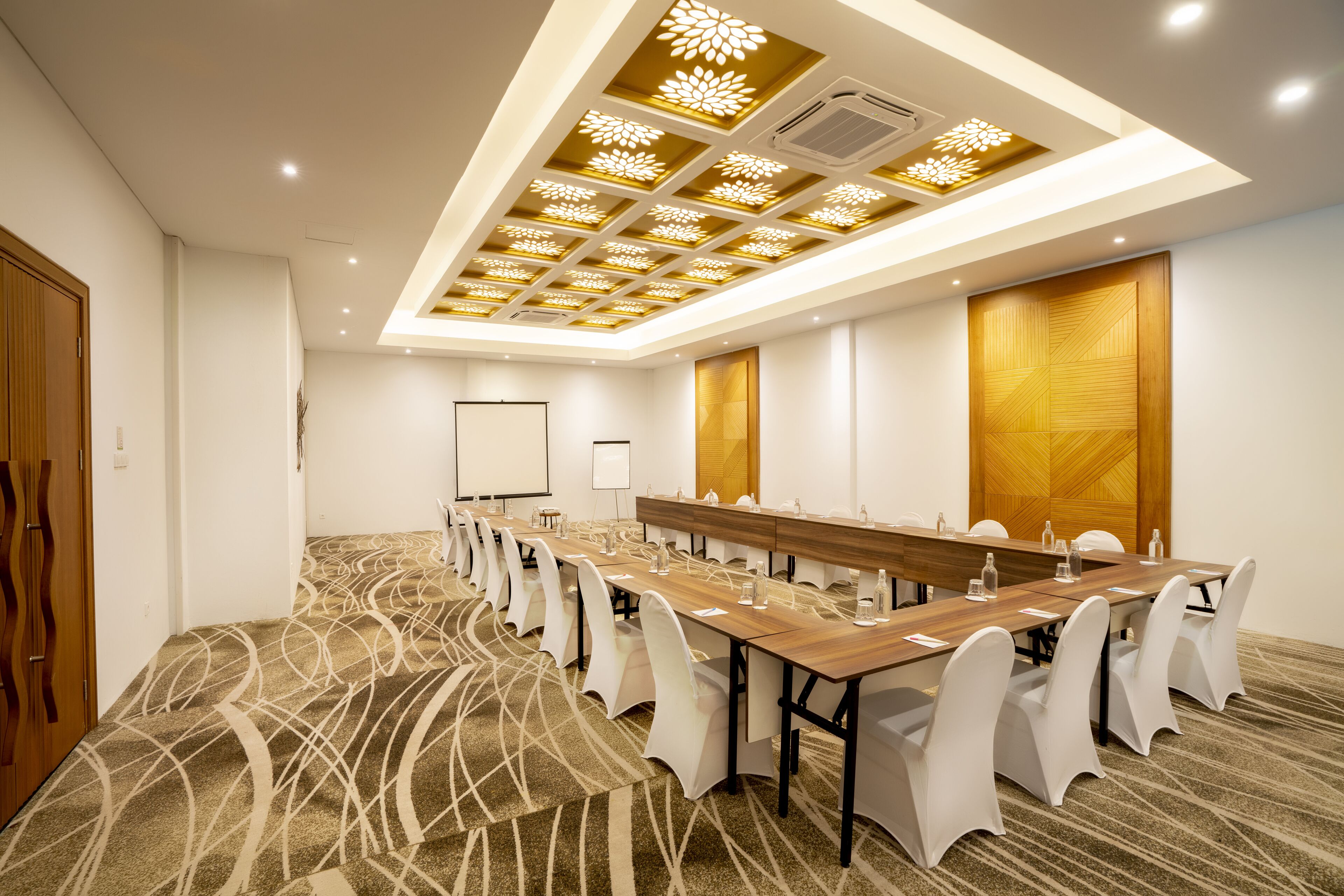 A conference room with a long table, white chairs, and a patterned carpet.
