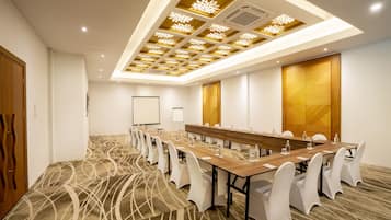 A conference room with a long table, white chairs, and a patterned carpet.