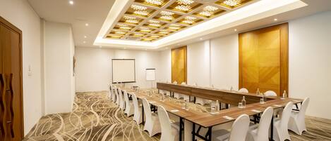 A conference room with a long table, white chairs, and a patterned carpet.