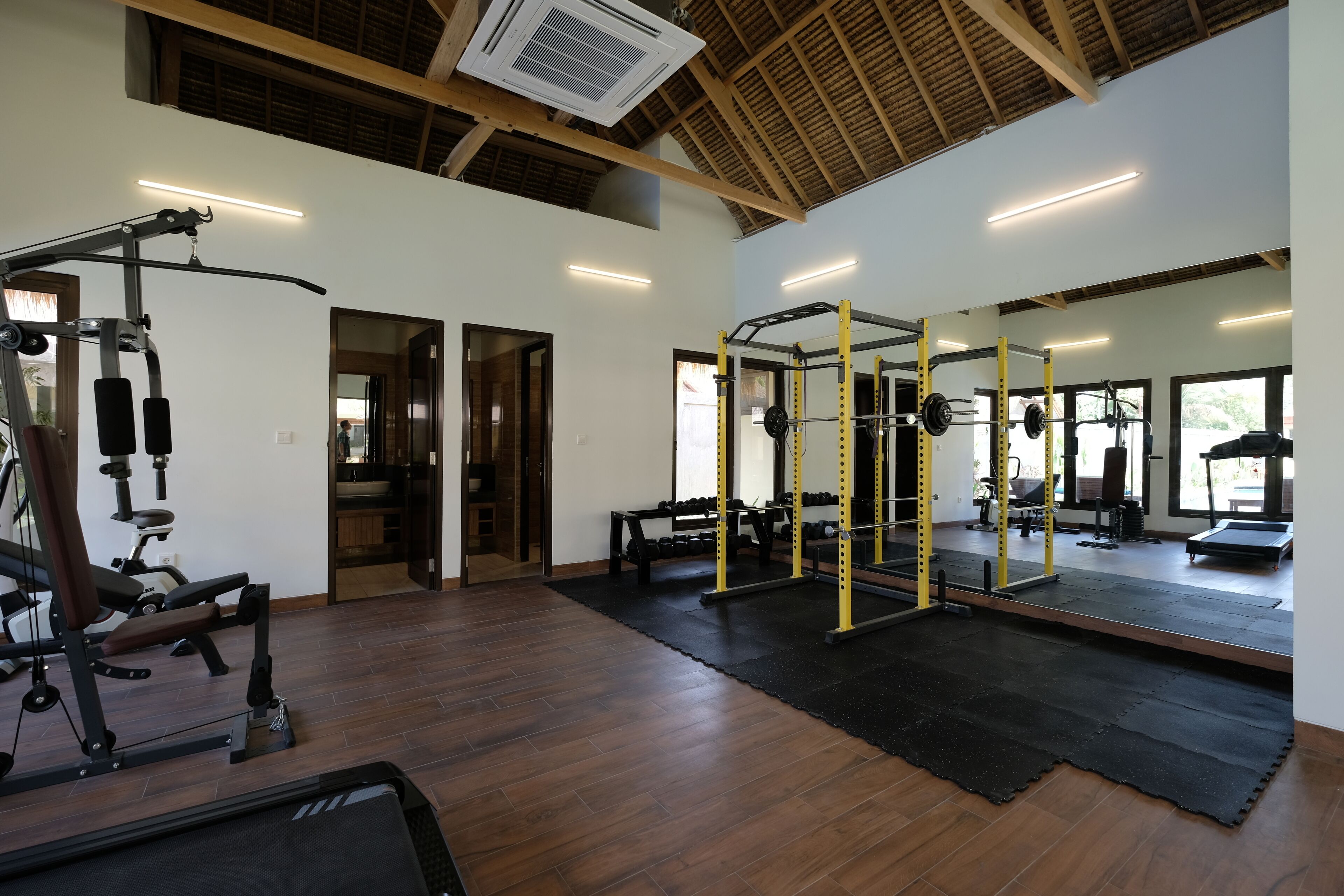 A gym with wooden floors, exercise equipment, and large windows.
