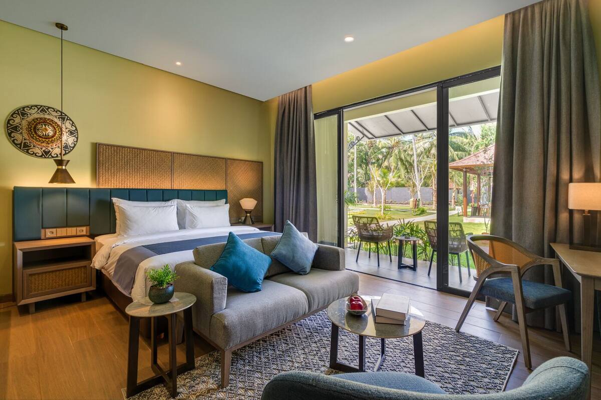 Ein modernes Hotelzimmer mit einem großen Bett, einer Sitzecke, einem kleinen Tisch und einem Balkon mit Sitzmöbeln.