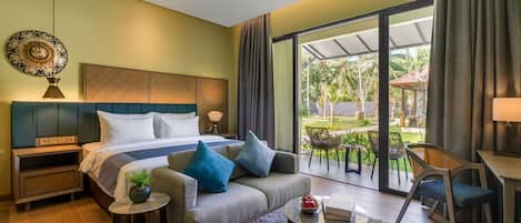 A modern hotel room with a large bed, a sofa, a small table, and a balcony with outdoor seating.