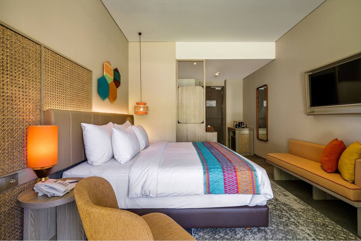 Ein modernes Hotelzimmer mit einem großen Bett, einer Couch, einem Schreibtisch mit Lampe und einem Fernseher.