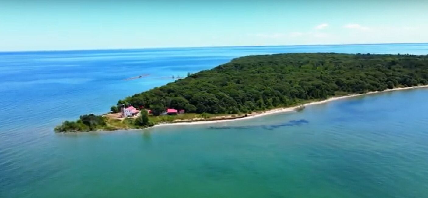 An aerial view of a coastal area with a small island featuring a few buildings and dense greenery.