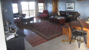 A living room with a brown leather sofa, a red armchair, a wooden coffee table, and a dining table with chairs. - Charity Island Lightkeepers Home Big Charity Island (Tawas)