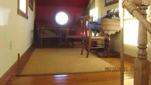A room with a wooden floor, a rug, a desk with a chair, a window, and a wooden railing. - Charity Island Lightkeepers Home Big Charity Island (Tawas)