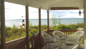 A covered porch with a view of the sea, featuring wicker chairs and a lantern. - Charity Island Lightkeepers Home Big Charity Island (Tawas)