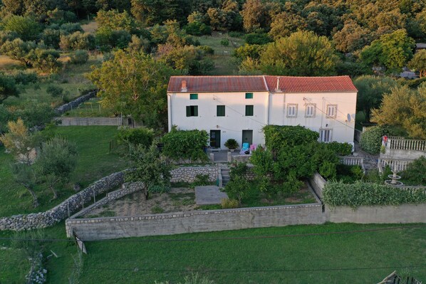 A two-story white building with a red roof, surrounded by greenery and a stone wall. - Vacation House Viskic (Supetarska Draga)