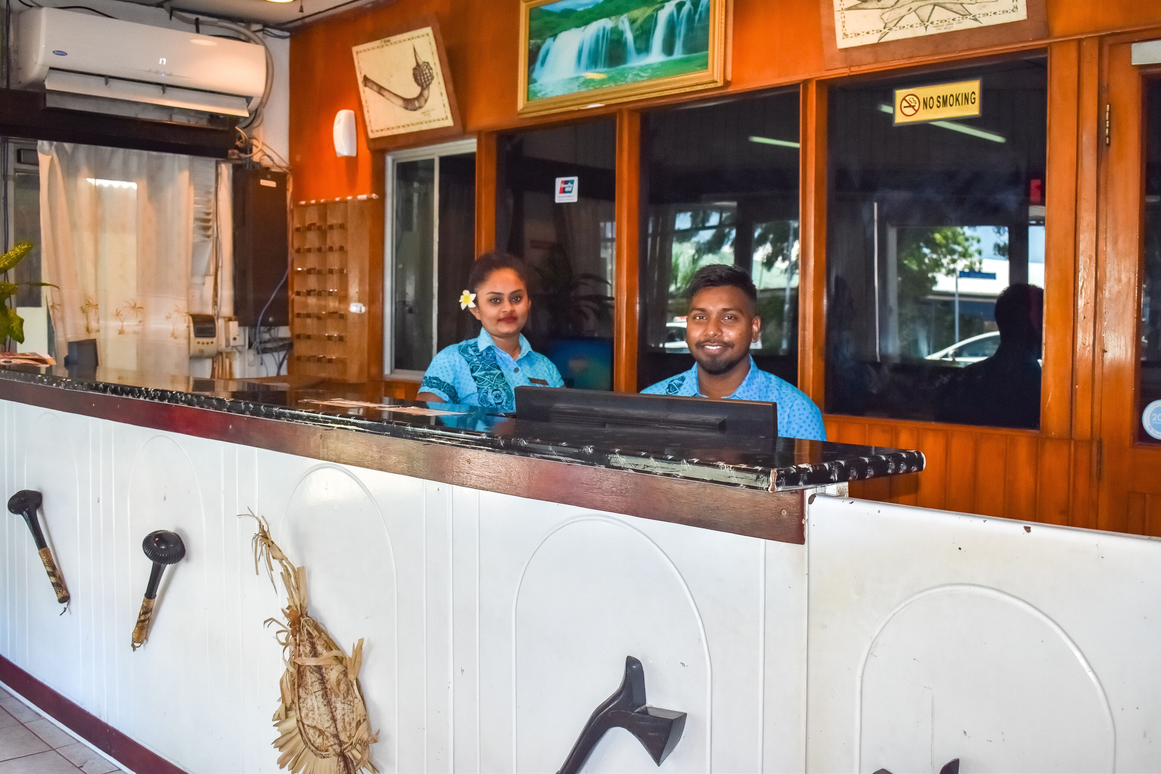 A reception desk with a wooden counter, a 'No Smoking' sign, and a framed picture of a waterfall.